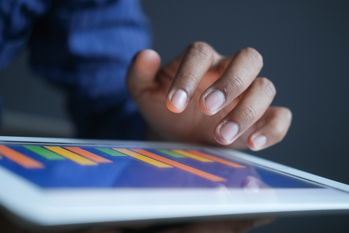 man's hand working on digital tablet at office desk, using self created chart.