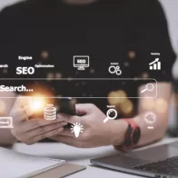 Profissional utilizando smartphone e notebook com ícones digitais representando SEO, dados e análise — conceito de marketing digital integrado.